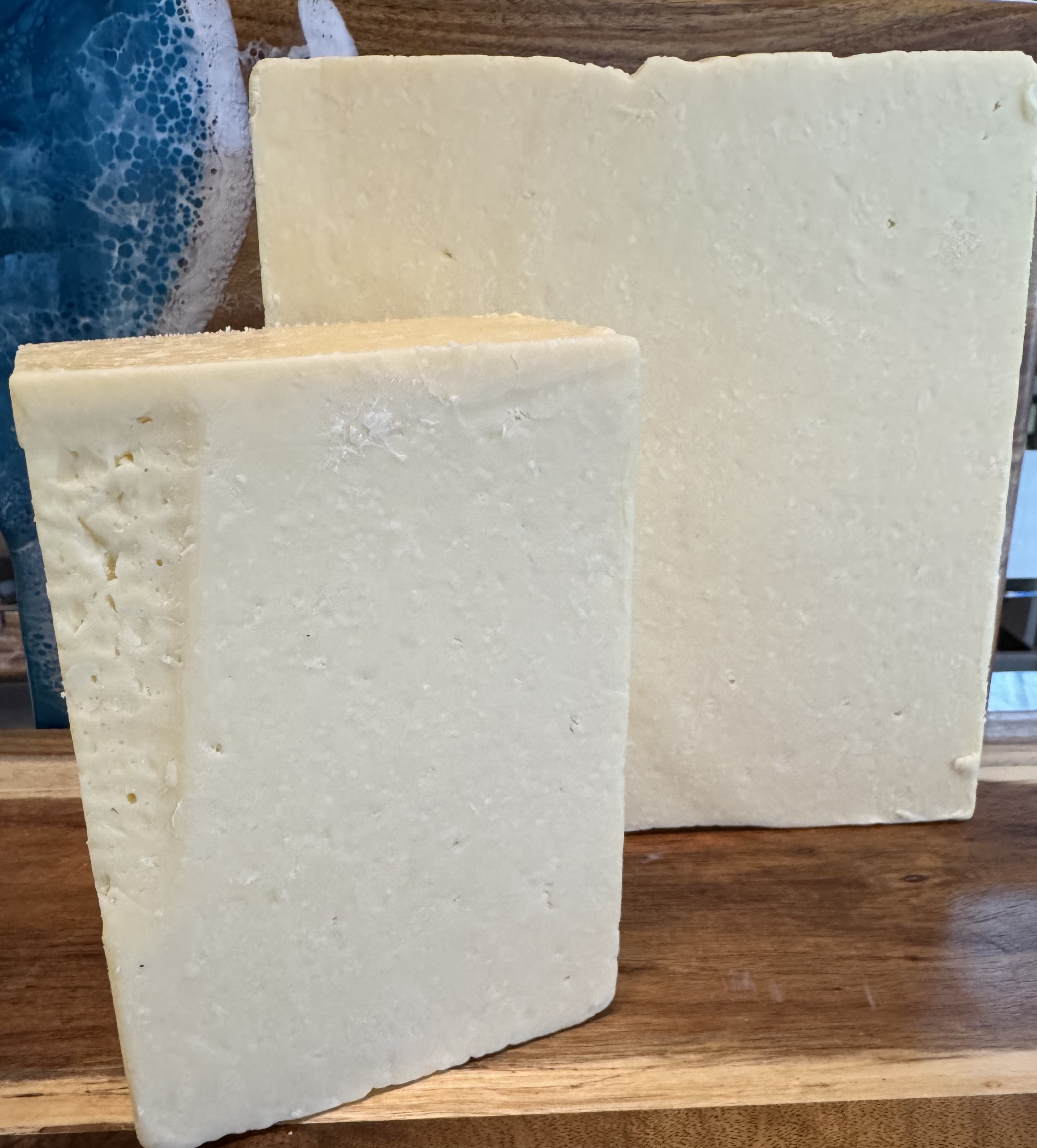 Two pale fresh-style cheese slabs on a wood board.